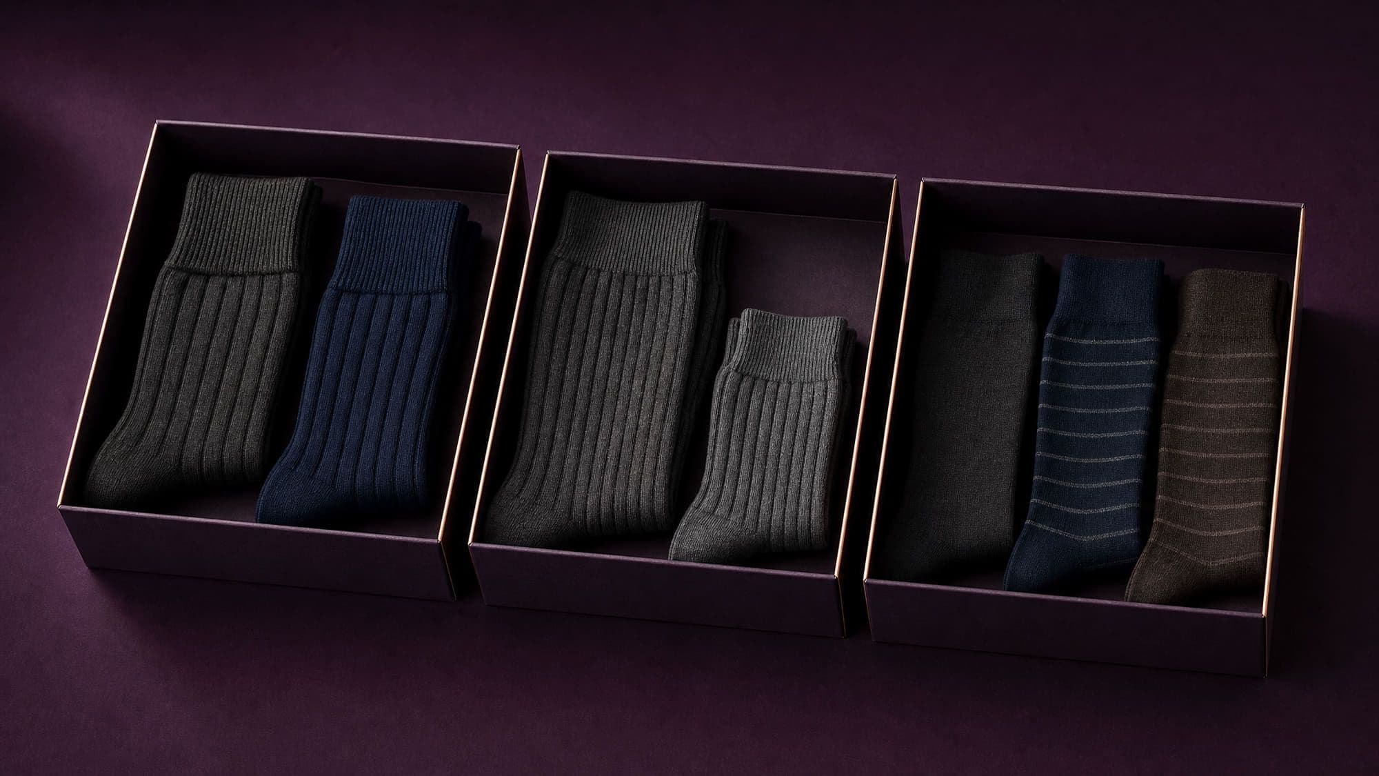 Three open gift boxes side by side: one with loose-cuff socks, one holding the same style in two sizes, one with three fine-knit pairs